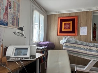 Cabinet de thérapie avec appareil de bioresonance sur un bureau, table de massage, et chartes anatomiques. Ambiance calme et professionnelle.